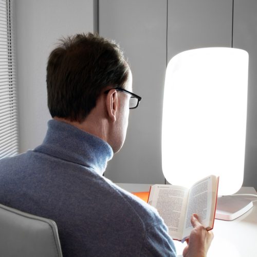 Man reading next to light therapy lamp