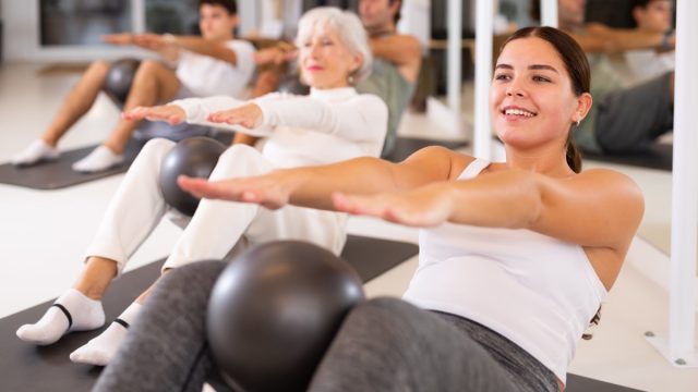 Adult people different ages practicing pilates with ball at group class in yoga studio