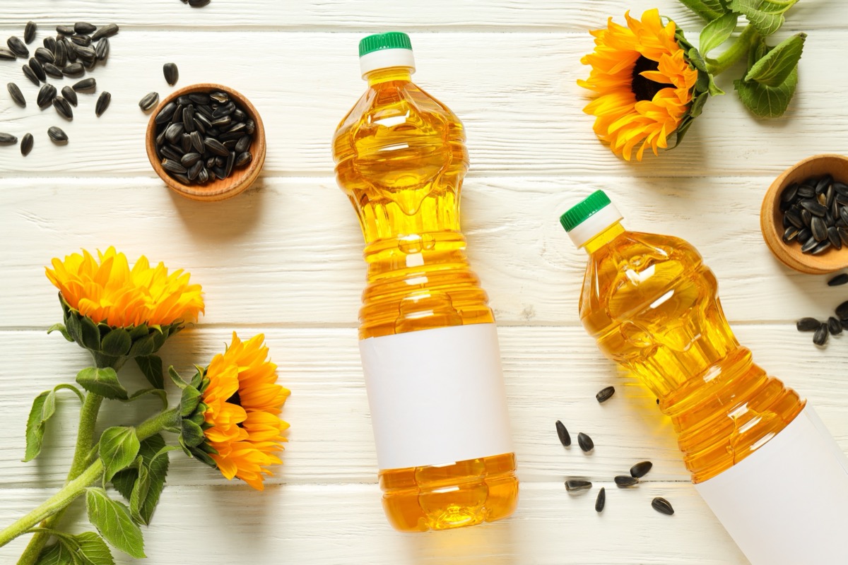 Sunflower oil and sunflowers on white wooden background