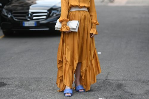 Street style outfit, woman wearinga leather belt, a long yellow mustard dress, a white clutch and block heels sandals on the streets of Milan, Italy.