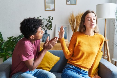 man and woman sitting on a couch. he's pleading with her while she holds her hand up in his face