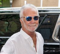 Captain Lee Rosbach wearing a white shirt and sunglasses standing in front of a black SUV