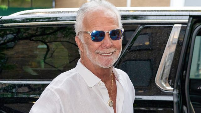 Captain Lee Rosbach wearing a white shirt and sunglasses standing in front of a black SUV