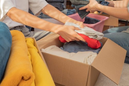 Woman and child sorting clothes and packing into cardboard box. Donations for charity, help low income families, declutter home, sell online, moving moving into new home, recycling, sustainable living