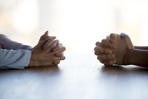 close up of two pairs of hands, each clasped, sitting across each other at a table
