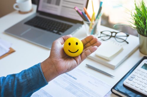 man holding an emoticon ball in front of his work desk