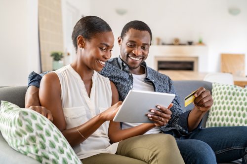 wife doing shopping online while using digital tablet at home with husband. Couple using bank card to pay bills or to book their next vacation. Mature couple making an online purchase.