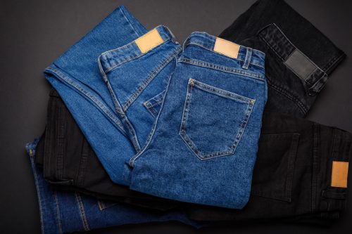 Blue denim jeans on pile of jeans pants. Top view of variety of denim jean textiles on black background. Many jean trousers pants.