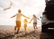 A family of three running on the beach next to their car