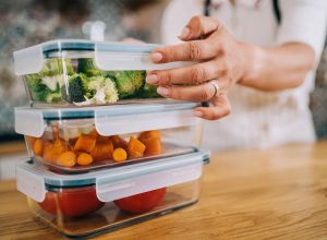Close-up shot of female hands holding glass containers with fresh raw vegetables.