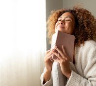 Happy woman dressed in beige smiling with her eyes closed while holding a journal