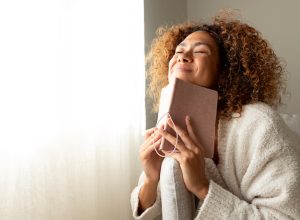 Happy woman dressed in beige smiling with her eyes closed while holding a journal