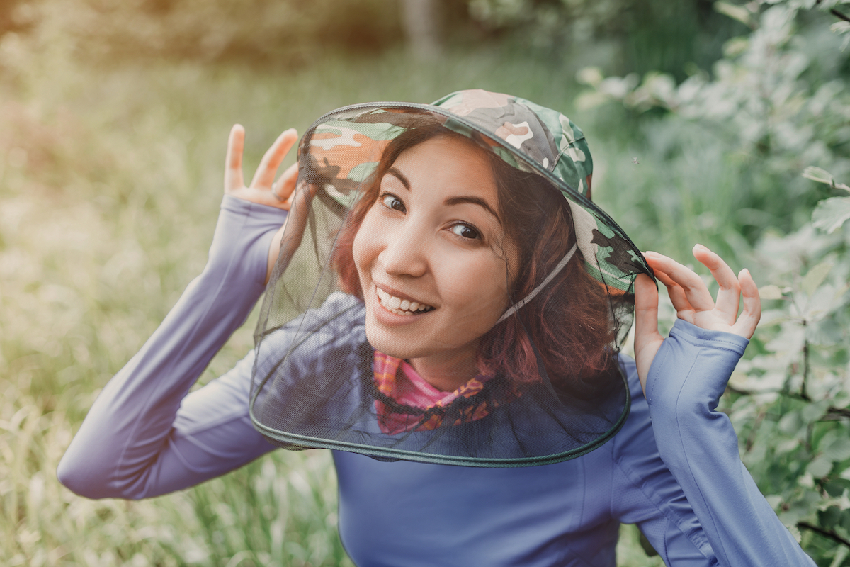Happy girl in a hat with an anti-mosquito net in the forest