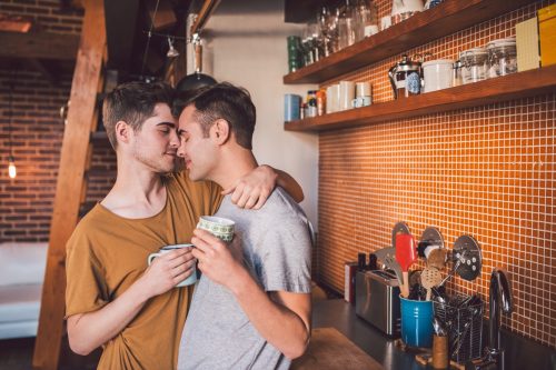 Two men embracing and holding coffee mugs in a kitchen
