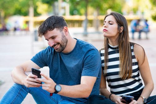 Woman looking over man's shoulder as he reads his smartphone