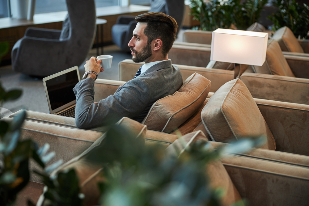 A man drinking coffee while working on a laptop in an airport lounge