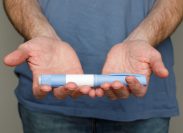 Close up of a man in a blue t-shirt holding out a Semaglutide or Ozempic pen
