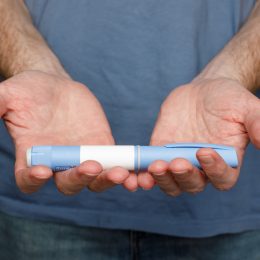 Close up of a man in a blue t-shirt holding out a Semaglutide or Ozempic pen