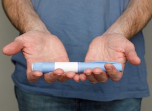 Close up of a man in a blue t-shirt holding out a Semaglutide or Ozempic pen