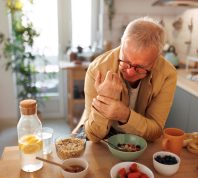 Senior man experiencing hand joint pain while having breakfast in the kitchen