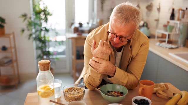 Senior man experiencing hand joint pain while having breakfast in the kitchen