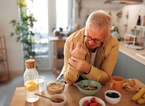 Senior man experiencing hand joint pain while having breakfast in the kitchen