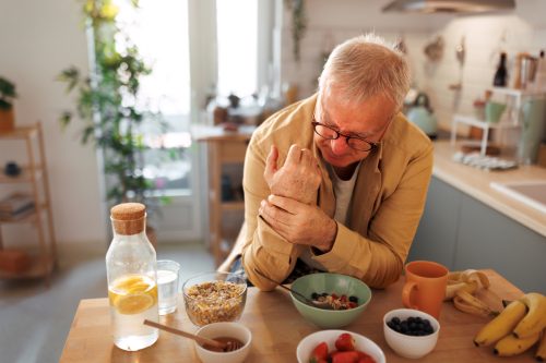 Senior man experiencing hand joint pain while having breakfast in the kitchen