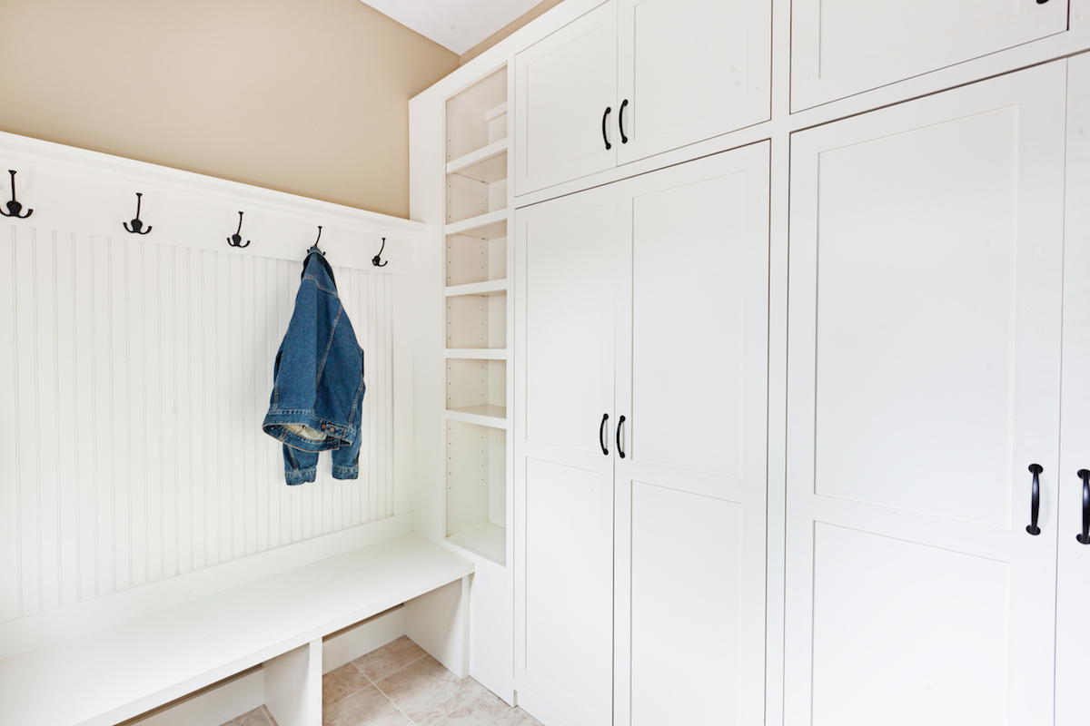 A newly remodeled back door entry way with mudroom with built-in storage painted cabinet closet in white. The room is featuring coat hangers wall, with shoes storage and seating facilities and tile floor. Photographed in horizontal format.