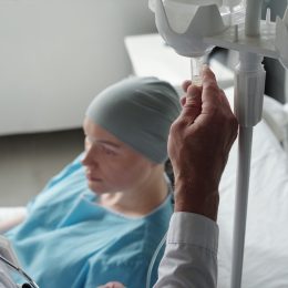 Close-up of mature male oncologist preparing dropper for chemotherapy before procedure while standing by bed with sick female patient