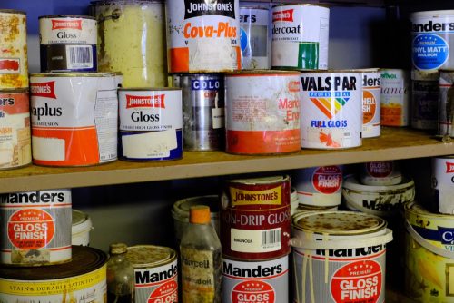 A collection of old paint tins of various sizes on two shelves.