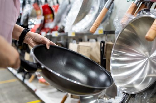 Hands of girl holding a new pan,choosing black teflon frying pan,asian customer deciding to buy non-stick frying pan for cooking food in her kitchen,shopping cookware household goods at supermarket