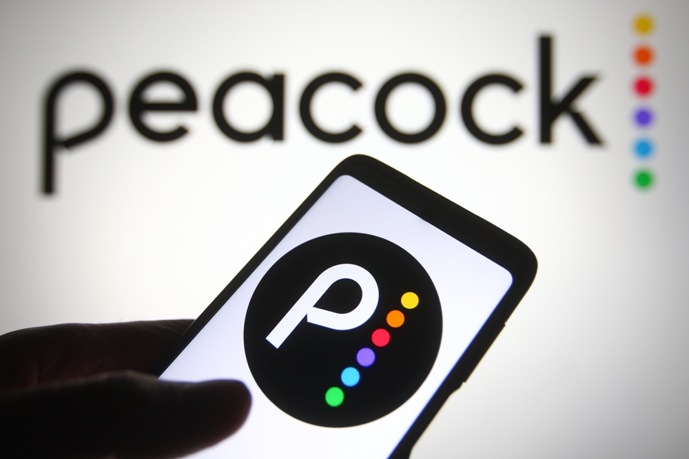 The Peacock logo on a phone in front of it printed on a wall