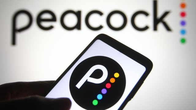 The Peacock logo on a phone in front of it printed on a wall