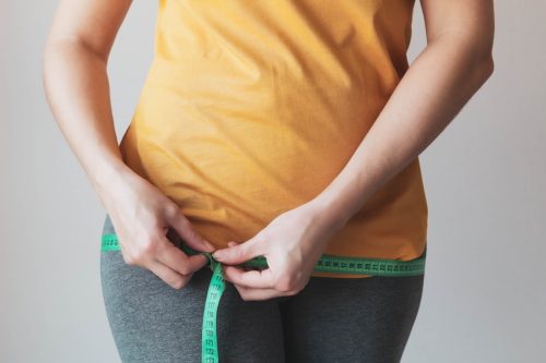 The woman measures the volume of the hips with a green measuring tape.