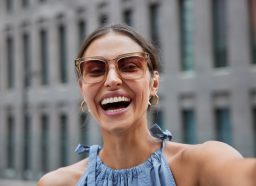 portrait of a happy, laughing woman taking a selfie while outside on a city street wearing oversized sunglasses