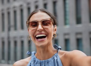 portrait of a happy, laughing woman taking a selfie while outside on a city street wearing oversized sunglasses