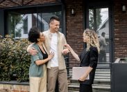 Realtor giving house key to a happy couple outside of a home