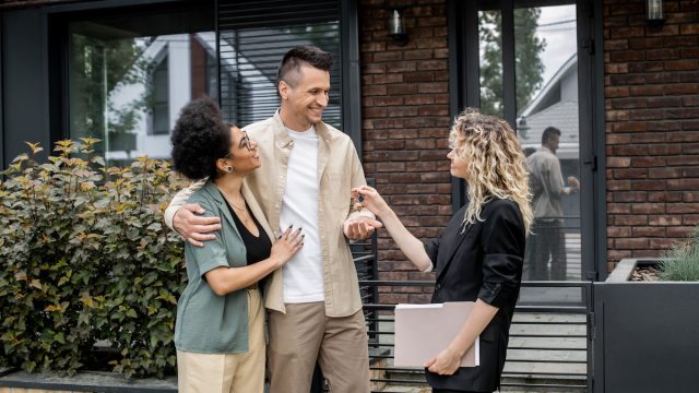 Realtor giving house key to a happy couple outside of a home