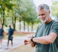 A senior man looking at his smartwatch and smiling during a run
