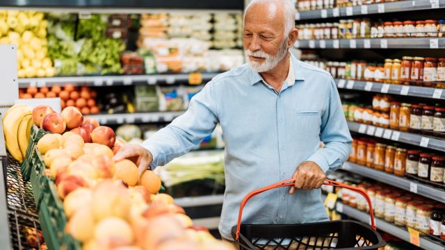 A senior man looking at fruit while shopping for groceries in a supermarket