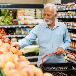 A senior man looking at fruit while shopping for groceries in a supermarket