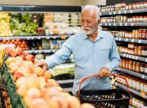 A senior man looking at fruit while shopping for groceries in a supermarket