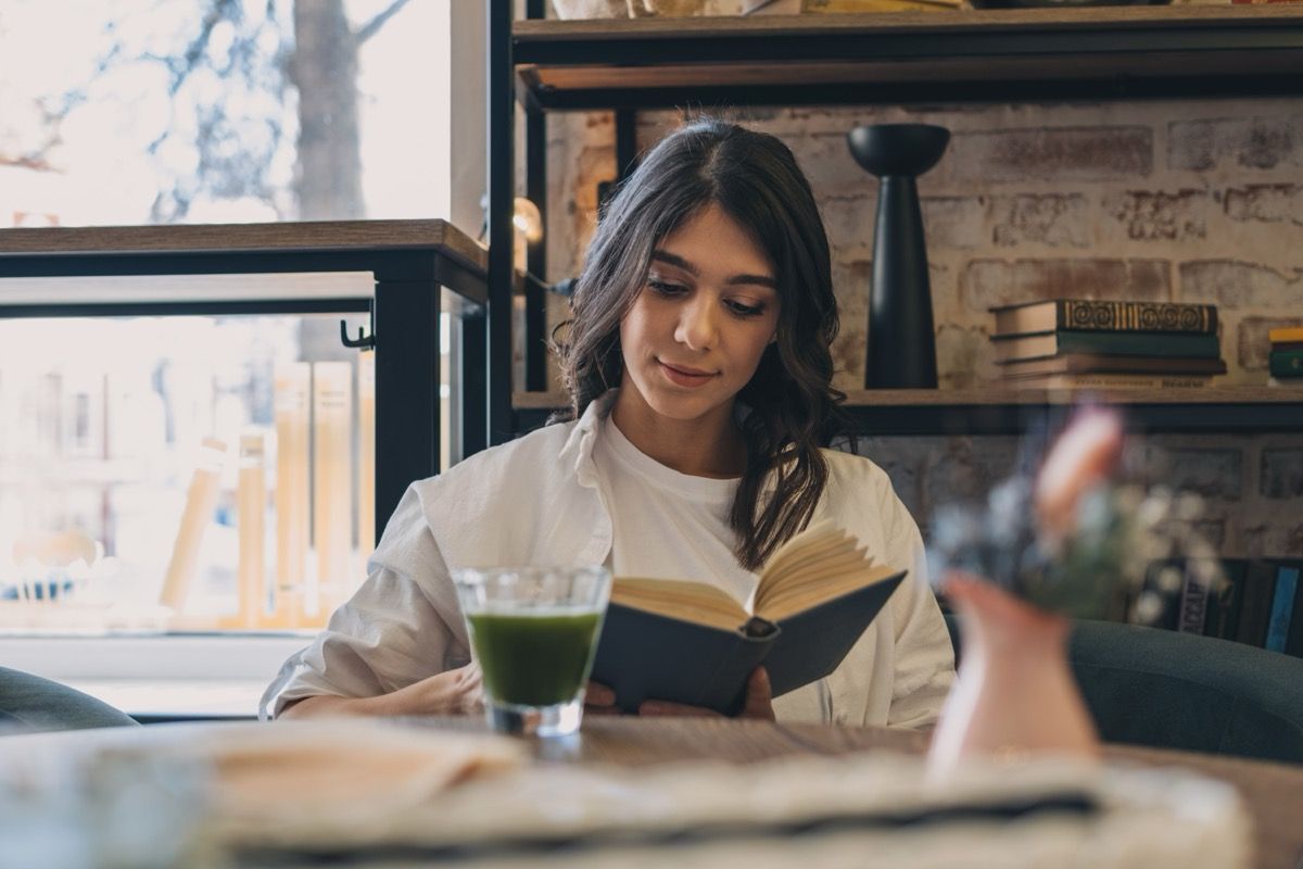 woman drinking matcha latte and reading at cafe