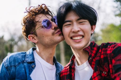 man kissing boyfriend's cheek as he smiles into the camera