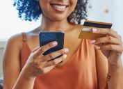 cropped portrait of a smiling woman wearing a rust-colored tank holding her iPhone and a credit card