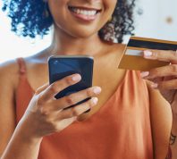 cropped portrait of a smiling woman wearing a rust-colored tank holding her iPhone and a credit card