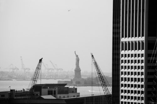 two cranes next to a skyscraper with the statue of liberty in the background