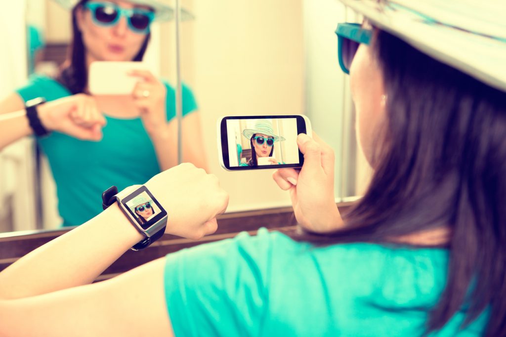 A woman taking a photo with her phone while using a smartwatch as a remote