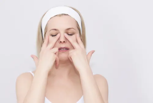 woman doing a face yoga exercise, touching the corners of her eyes, against a gray background