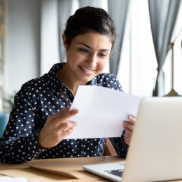 A woman smiling while reading a letter at her desk